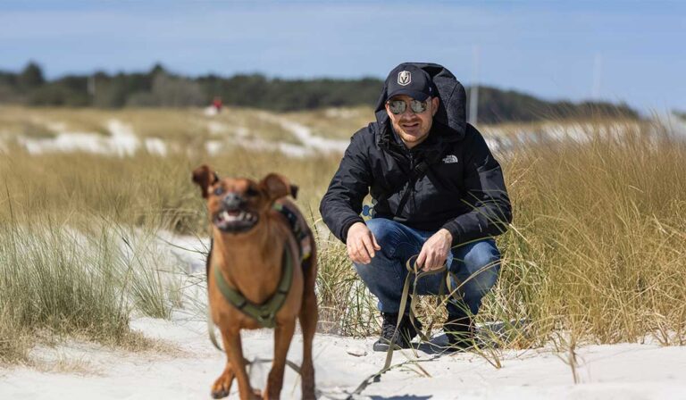 Ein Hund rennt mit seinem Besitzer an der Ostsee, abgesichert durch eine Hunde-OP-Versicherung.